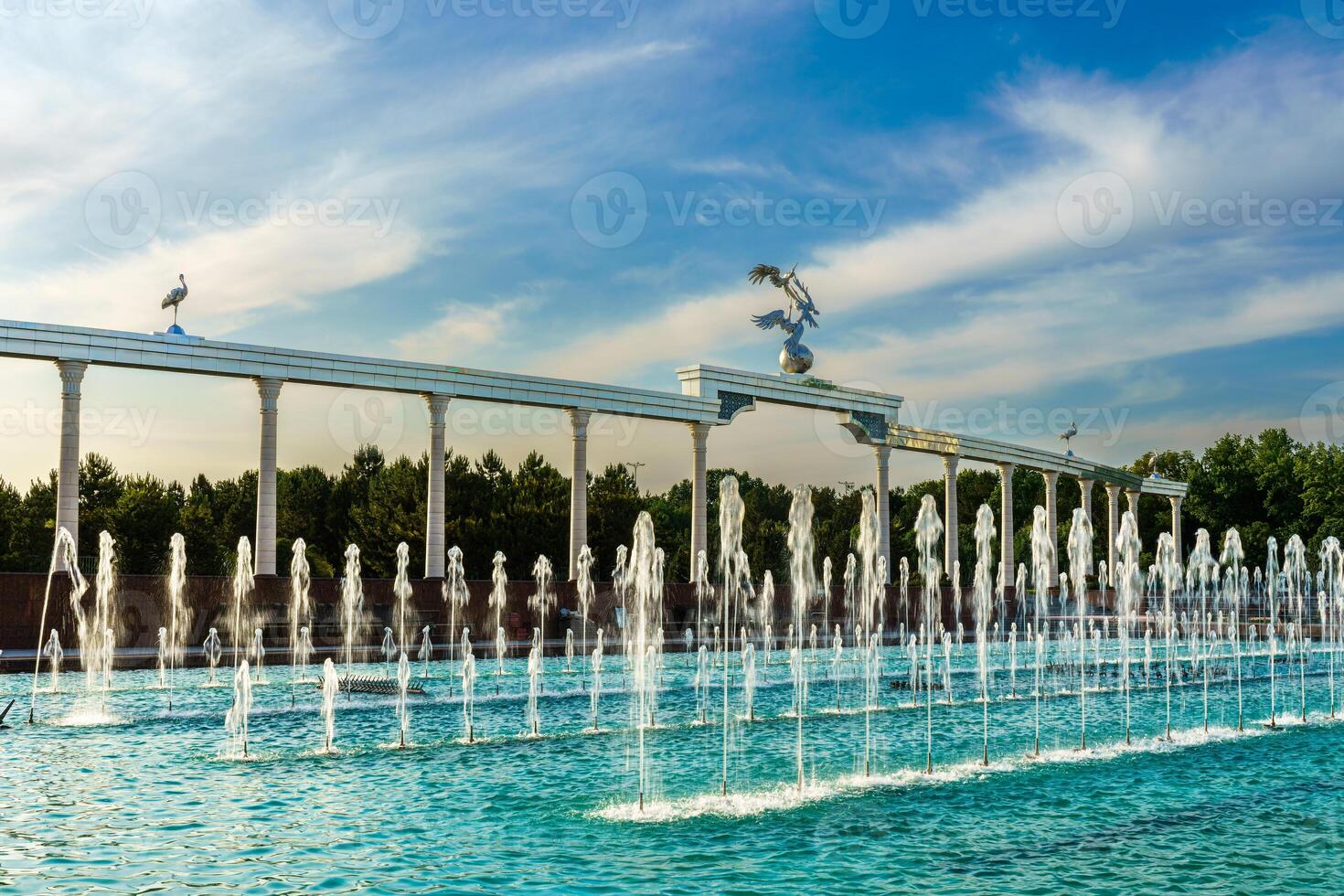 Memorial and rows of fountains illuminated by sunlight at sunset or sunrise in the Independence Square at summertime, Tashkent. photo