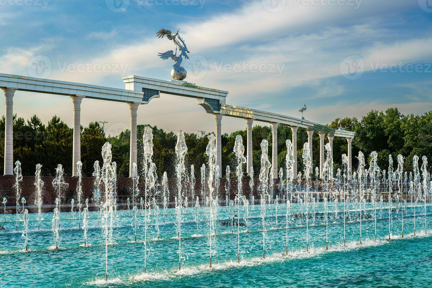 monumento y filas de fuentes iluminado por luz de sol a puesta de sol o amanecer en el independencia cuadrado a Hora de verano, Taskent. foto