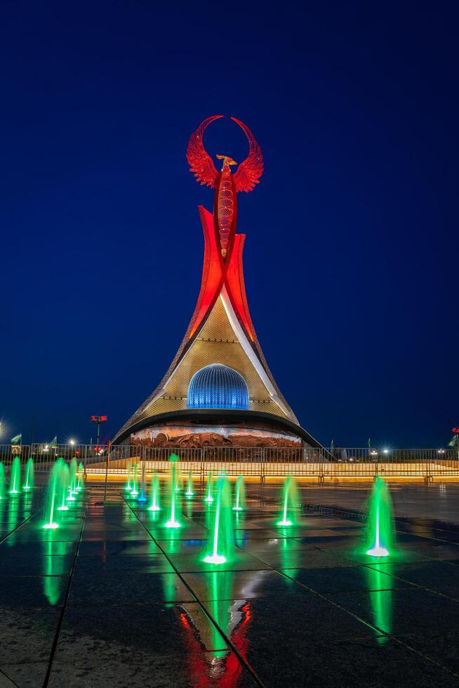 UZBEKISTAN, TASHKENT - MAY 5, 2023 Illuminated monument of independence in the form of a stele with a Humo bird, fountains and waving flags in the New Uzbekistan park at nighttime. photo