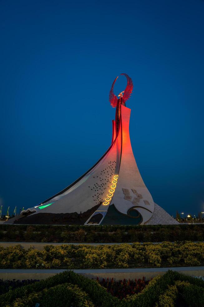 UZBEKISTAN, TASHKENT - MAY 5, 2023 Illuminated monument of independence in the form of a stele with a Humo bird, fountains and waving flags in the New Uzbekistan park at nighttime. photo