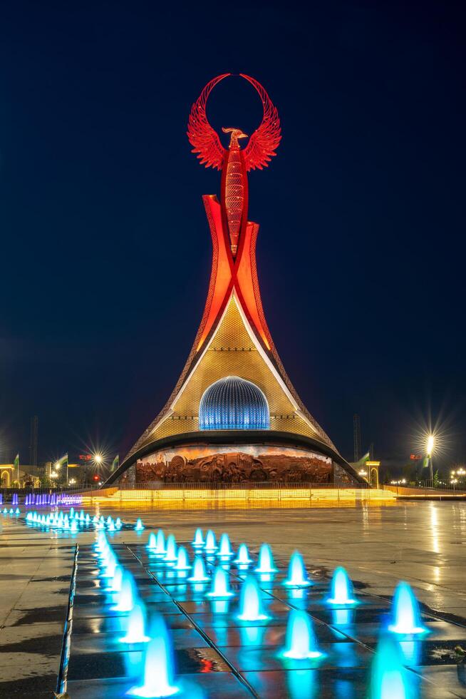 UZBEKISTAN, TASHKENT - MAY 5, 2023 Illuminated monument of independence in the form of a stele with a Humo bird, fountains and waving flags in the New Uzbekistan park at nighttime. photo