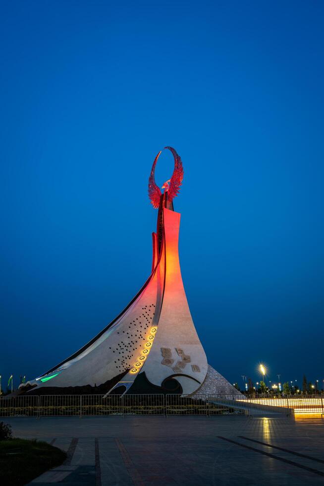 UZBEKISTAN, TASHKENT - MAY 5, 2023 Illuminated monument of independence in the form of a stele with a Humo bird, fountains and waving flags in the New Uzbekistan park at nighttime. photo