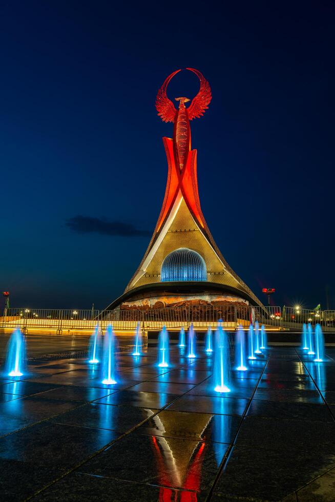UZBEKISTAN, TASHKENT - MAY 5, 2023 Illuminated monument of independence in the form of a stele with a Humo bird, fountains and waving flags in the New Uzbekistan park at nighttime. photo