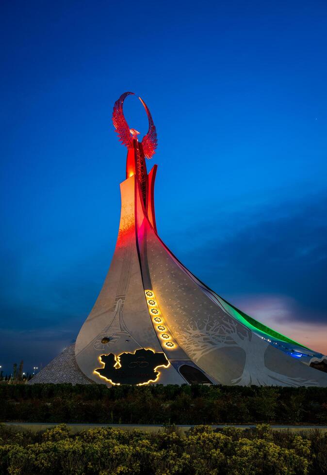 UZBEKISTAN, TASHKENT - MAY 5, 2023 Illuminated monument of independence in the form of a stele with a Humo bird, fountains and waving flags in the New Uzbekistan park at nighttime. photo