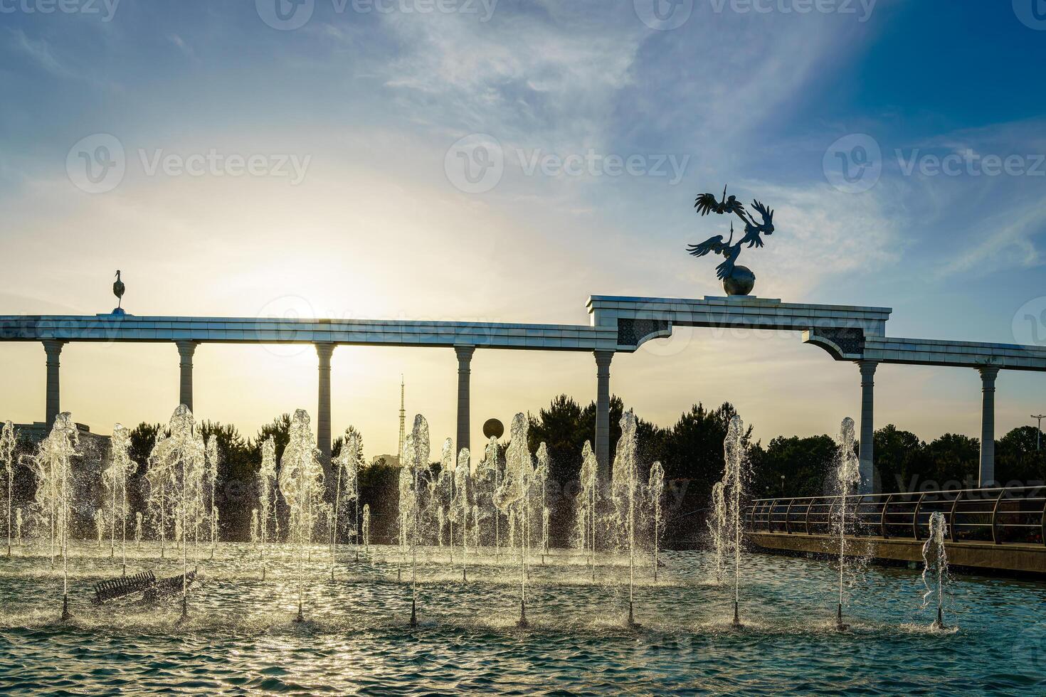 monumento y filas de fuentes iluminado por luz de sol a puesta de sol o amanecer en el independencia cuadrado a Hora de verano, Taskent. foto