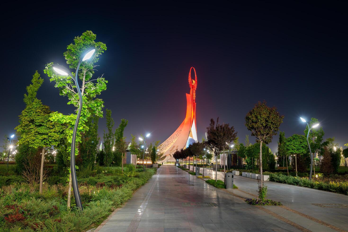 UZBEKISTAN, TASHKENT - MAY 5, 2023 Illuminated monument of independence in the form of a stele with a Humo bird, fountains and waving flags in the New Uzbekistan park at nighttime. photo