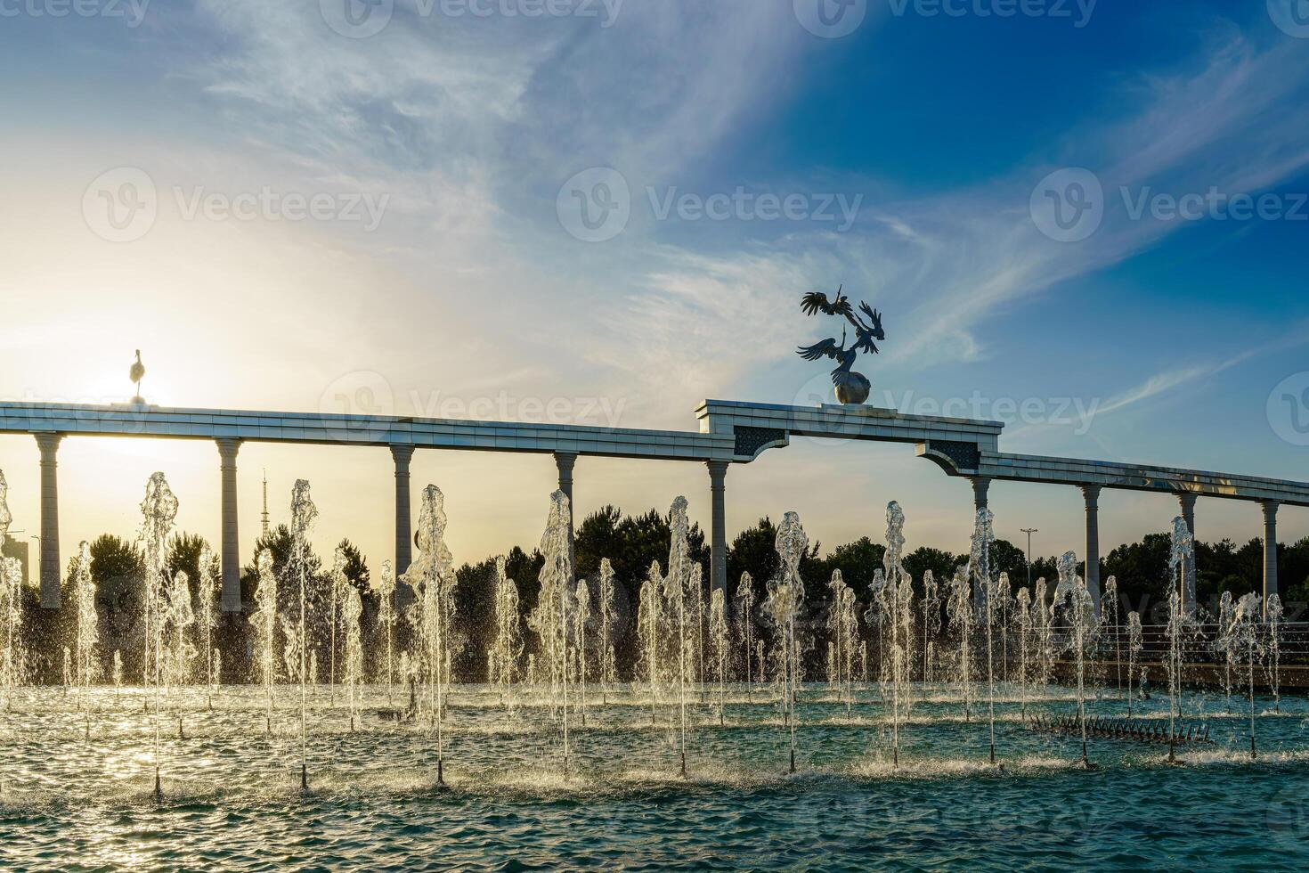 monumento y filas de fuentes iluminado por luz de sol a puesta de sol o amanecer en el independencia cuadrado a Hora de verano, Taskent. foto