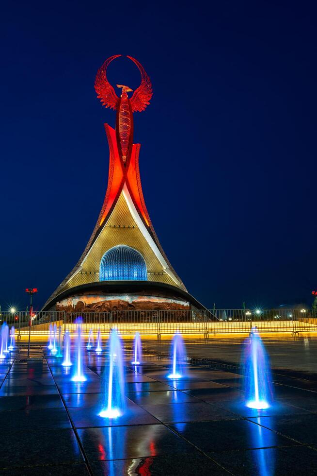 UZBEKISTAN, TASHKENT - MAY 5, 2023 Illuminated monument of independence in the form of a stele with a Humo bird, fountains and waving flags in the New Uzbekistan park at nighttime. photo