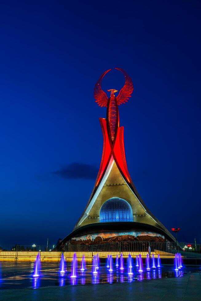 UZBEKISTAN, TASHKENT - MAY 5, 2023 Illuminated monument of independence in the form of a stele with a Humo bird, fountains and waving flags in the New Uzbekistan park at nighttime. photo