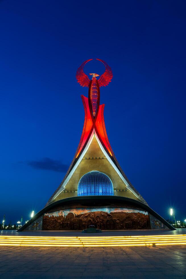UZBEKISTAN, TASHKENT - MAY 5, 2023 Illuminated monument of independence in the form of a stele with a Humo bird, fountains and waving flags in the New Uzbekistan park at nighttime. photo