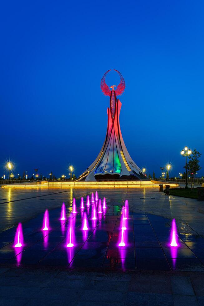 UZBEKISTAN, TASHKENT - MAY 25, 2023 Illuminated monument of independence in the form of a stele with a Humo bird and fountains in the New Uzbekistan park at nighttime. photo