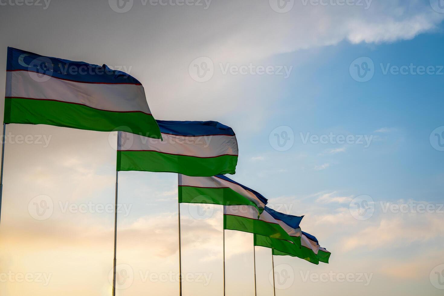 Flags of Uzbekistan waving on a sunset or sunrise dramatic sky background. photo