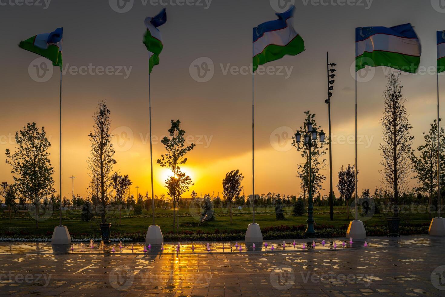 Flags of Uzbekistan waving on a sunset or sunrise dramatic sky background. photo