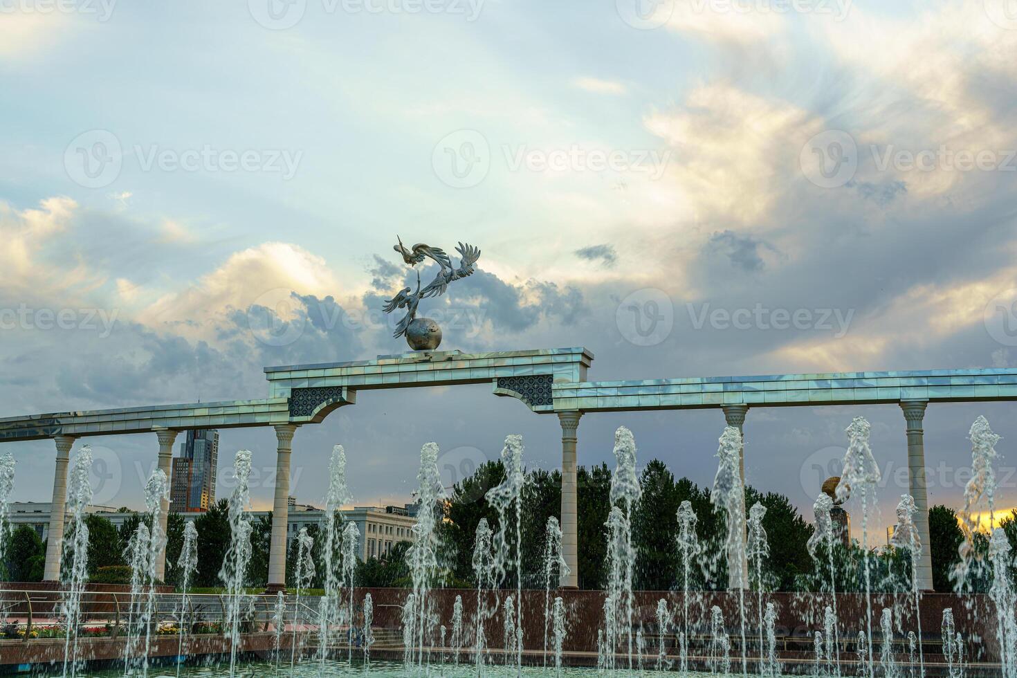 monumento y filas de fuentes iluminado por luz de sol a puesta de sol o amanecer en el independencia cuadrado a Hora de verano, Taskent. foto