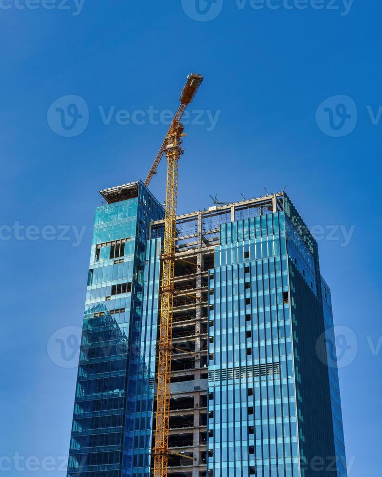 A crane building a skyscraper against a blue sky. photo