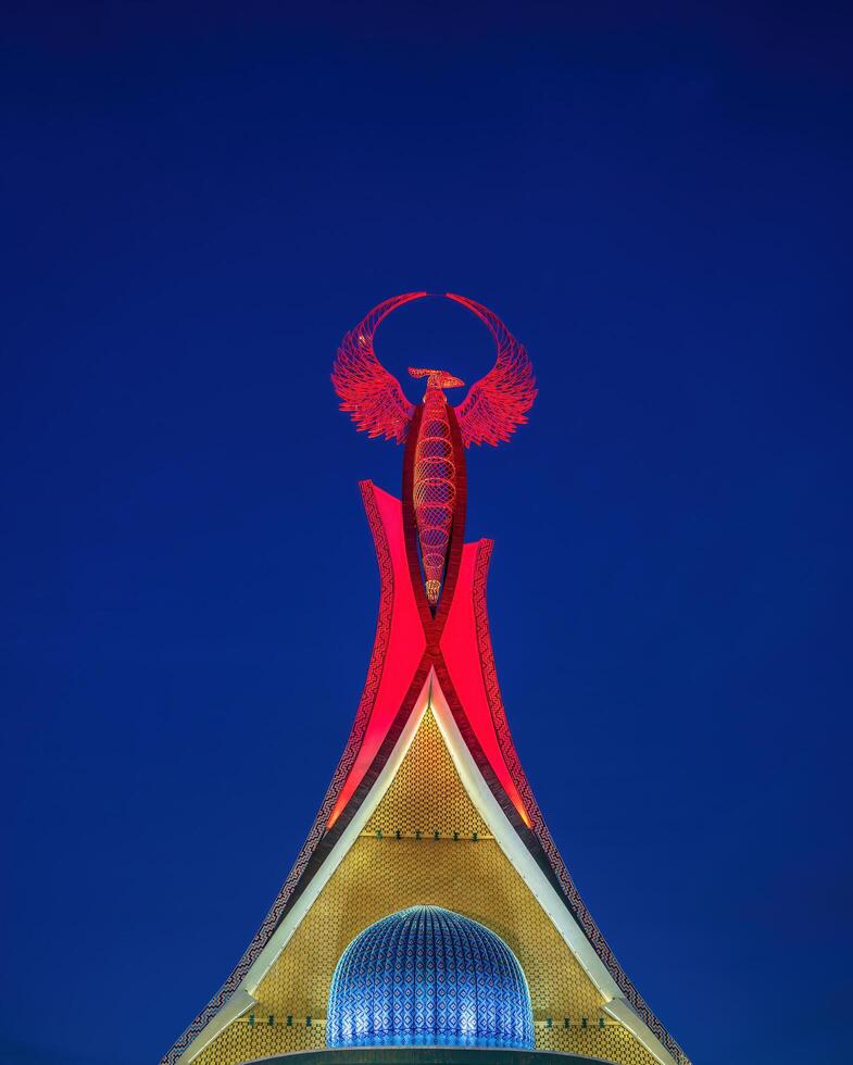 uzbekistán, Tashkent - enero 4, 2023 iluminado Monumento de independencia en el formar de un estela con un humo pájaro en el nuevo Uzbekistán parque a noche. foto