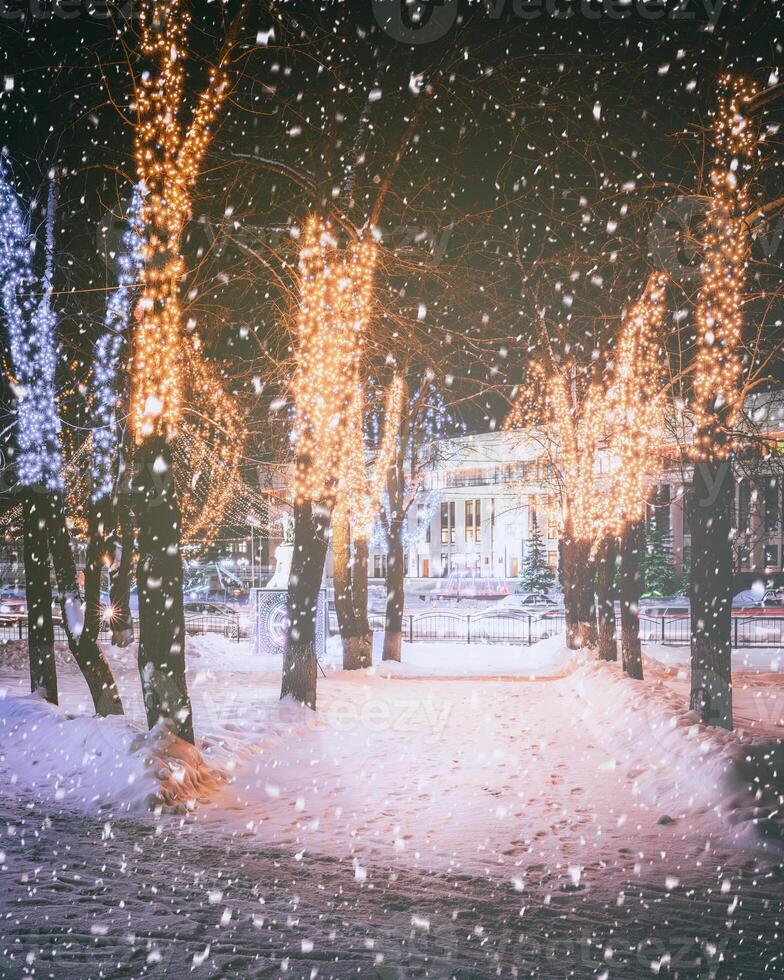 nevada en un invierno parque a noche con decoraciones, brillante linternas, pavimento cubierto con nieve y arboles Clásico película estético. foto