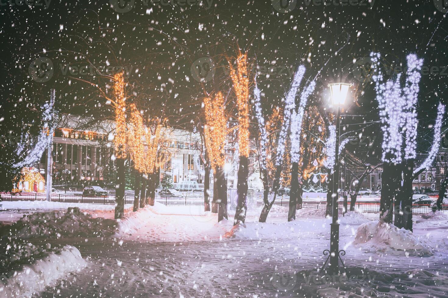 nevada en un invierno parque a noche con decoraciones, brillante linternas, pavimento cubierto con nieve y arboles Clásico película estético. foto