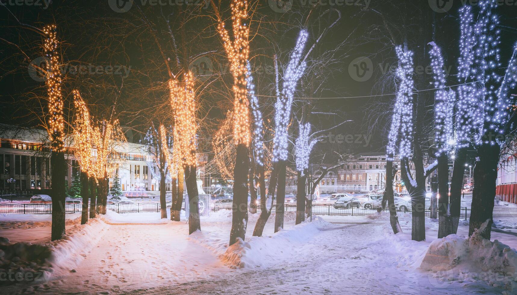 invierno parque a noche con Navidad decoraciones, brillante linternas, pavimento cubierto con nieve y arboles Clásico película estético. foto