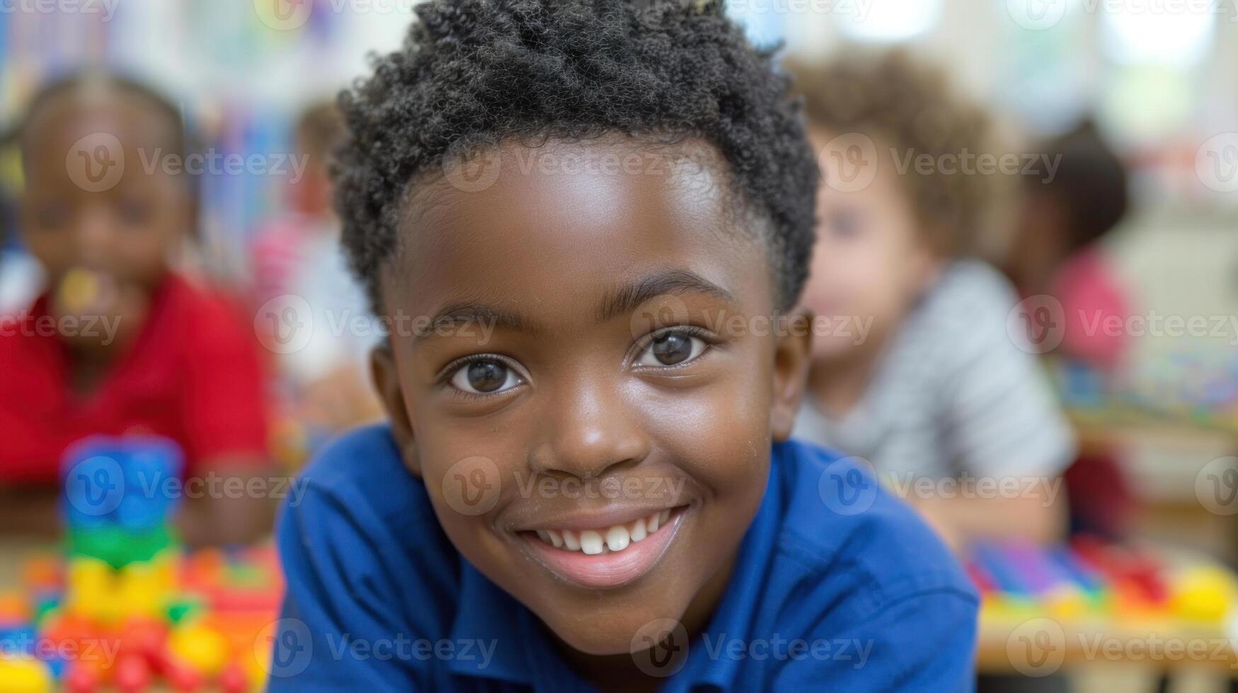 A young boy with a smile on his face looking directly at the camera in a classroom setting photo