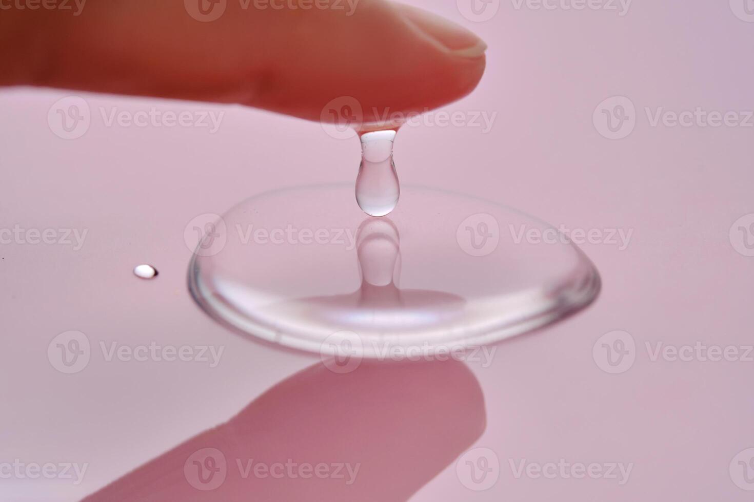 A finger touches a drop of cosmetic product on a pink background. photo