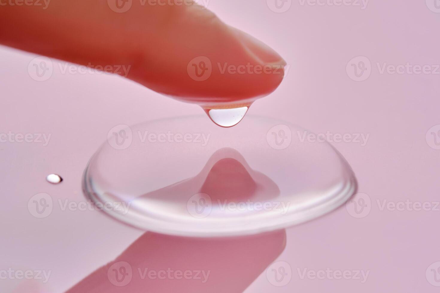 A finger touches a drop of cosmetic product on a pink background. photo