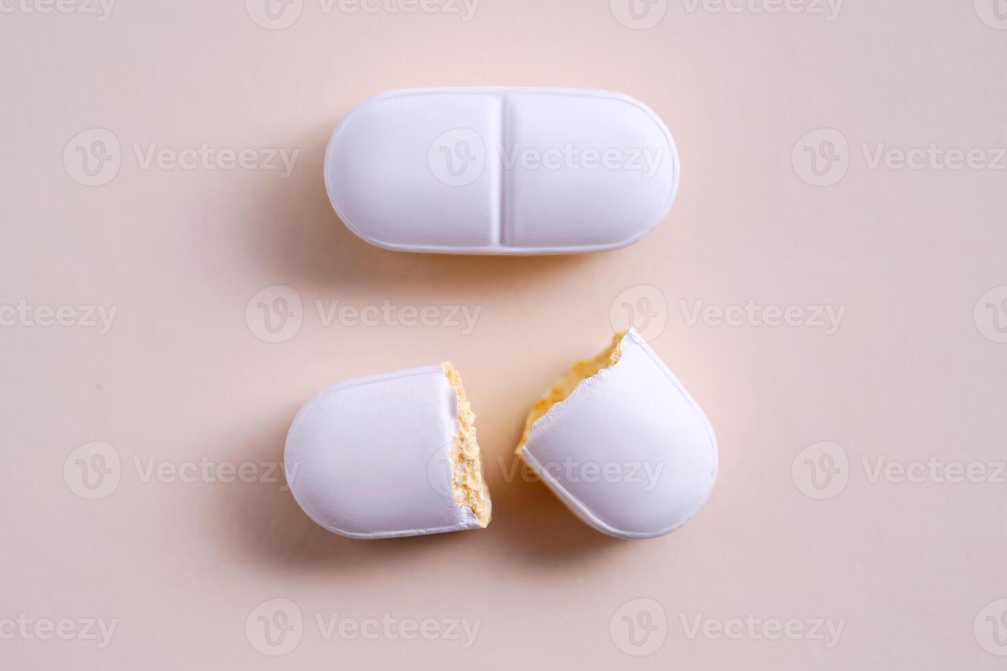 A whole and broken antibiotic tablet on a gray-pink background. photo