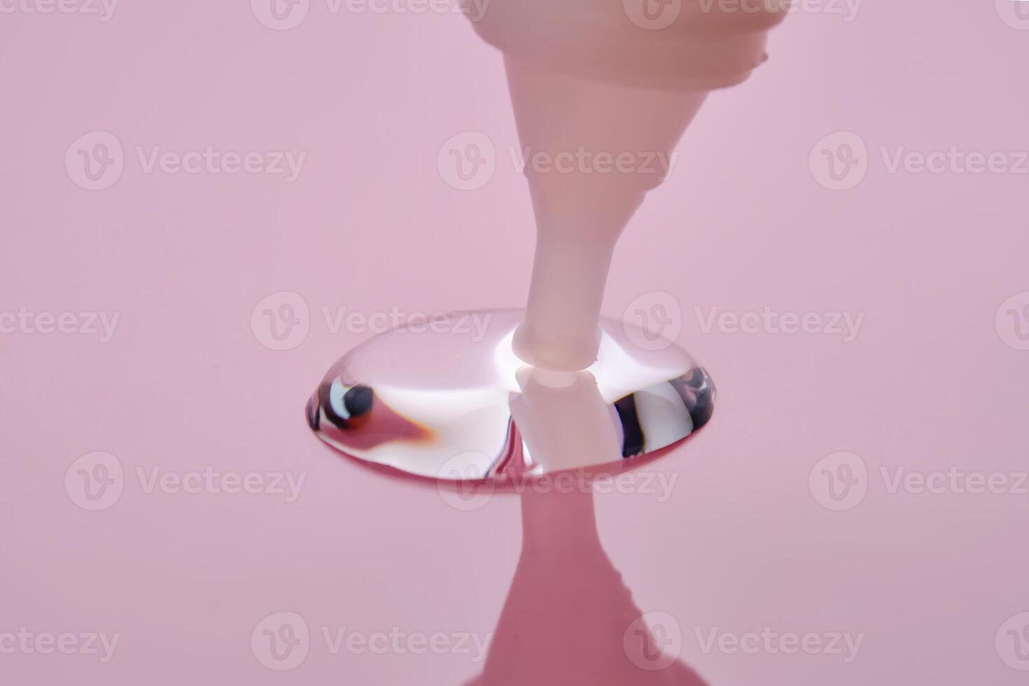 A drop of cosmetic product pours from a tube onto a pink background. photo