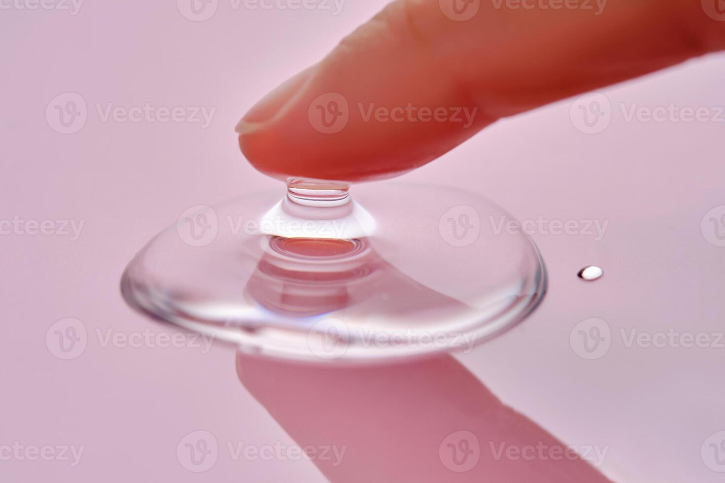 A finger touches a drop of cosmetic product on a pink background. photo