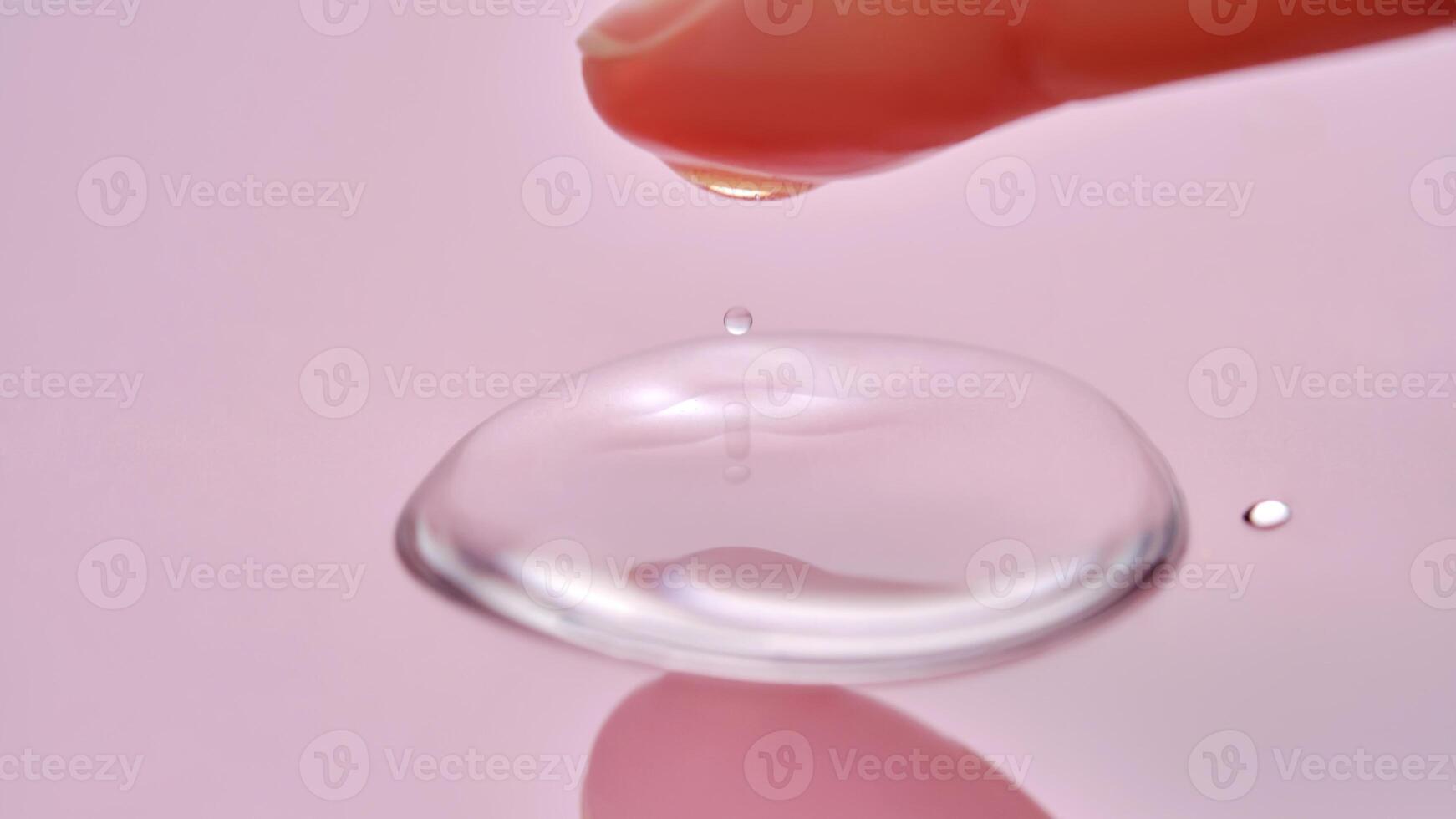 A finger touches a drop of cosmetic product on a pink background. photo