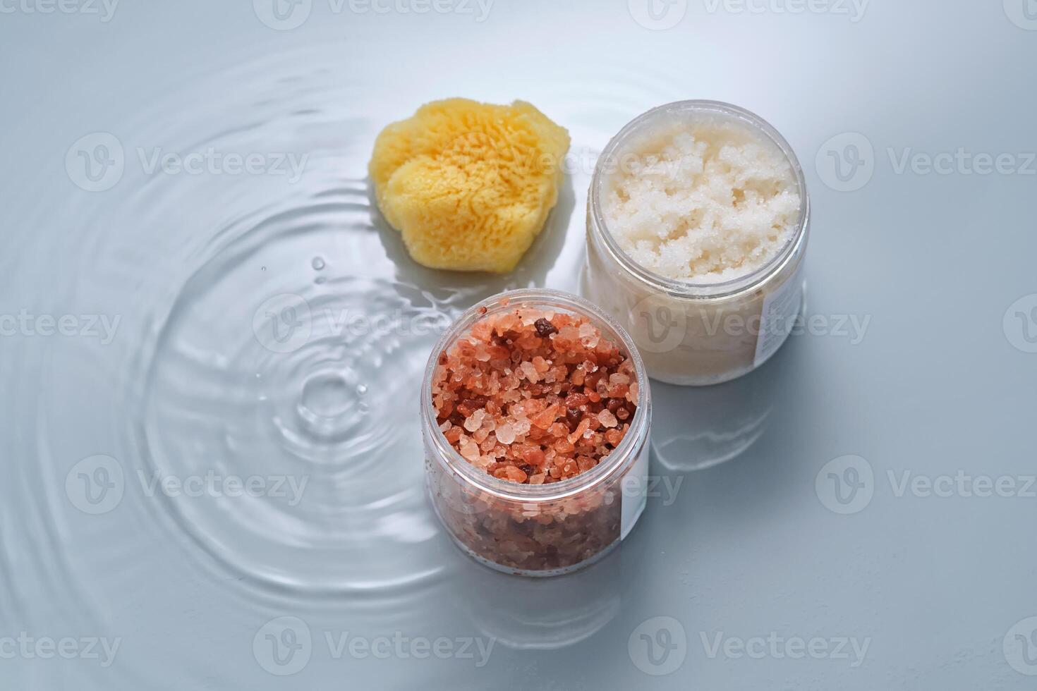 Body scrub, bath salt and natural sponge on a blue background with water. photo