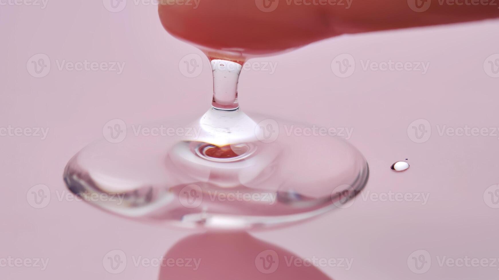 A finger touches a drop of cosmetic product on a pink background. photo