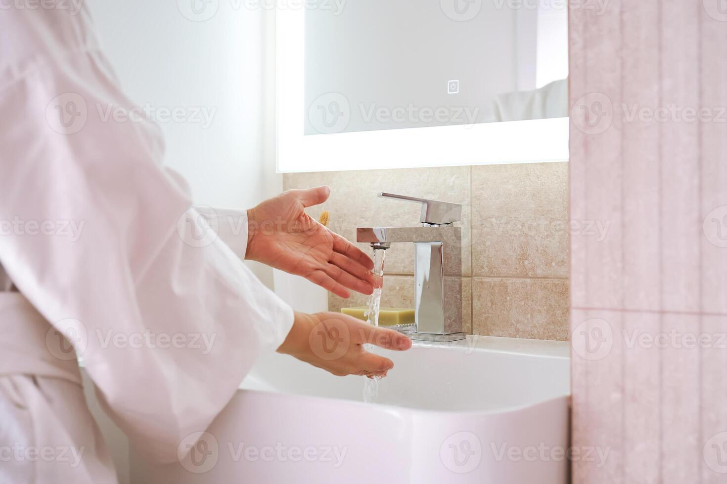 Women's hands under running water in the bathroom sink. photo