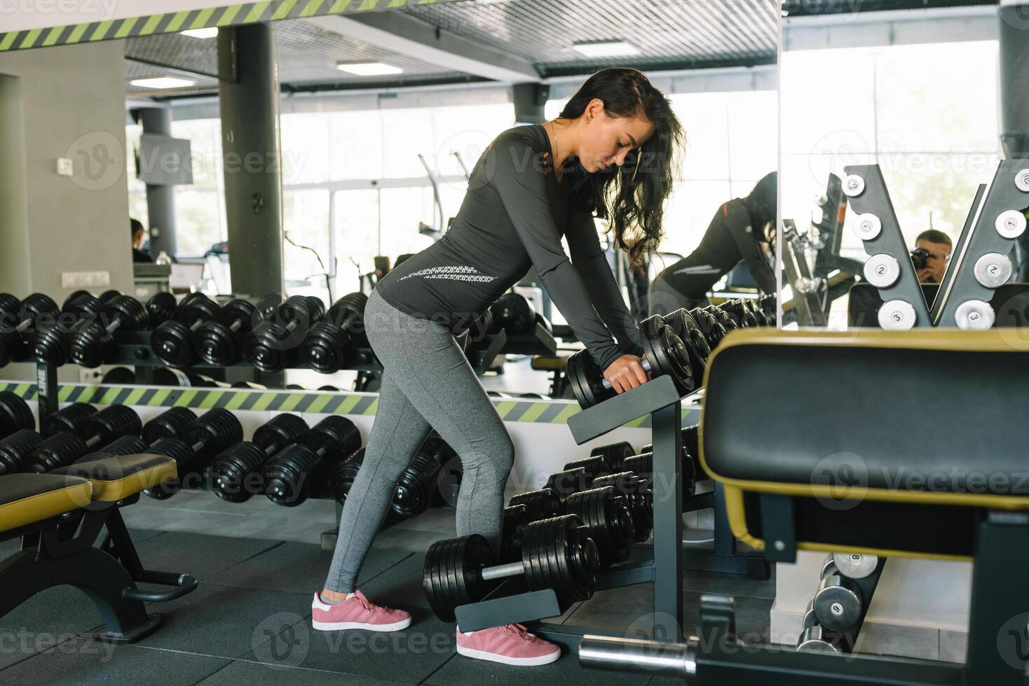 Gorgeous brunette lifting some weights and working on her biceps in a gym. photo