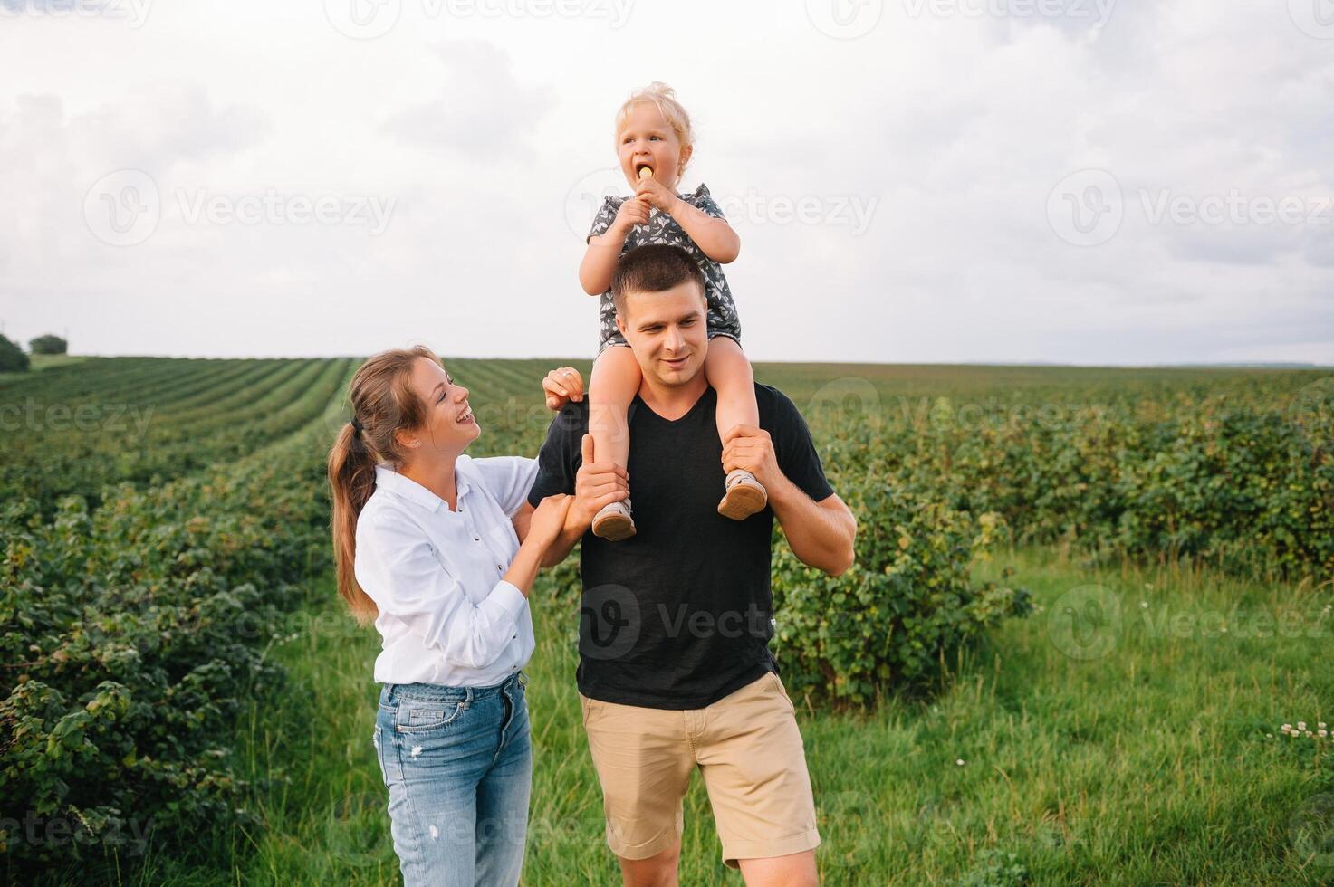 Happy family walking in the park. Mom, dad and daughter walk outdoors, parents holding the baby girl's hands. Childhood, parenthood, family bonds, marriage concept. photo