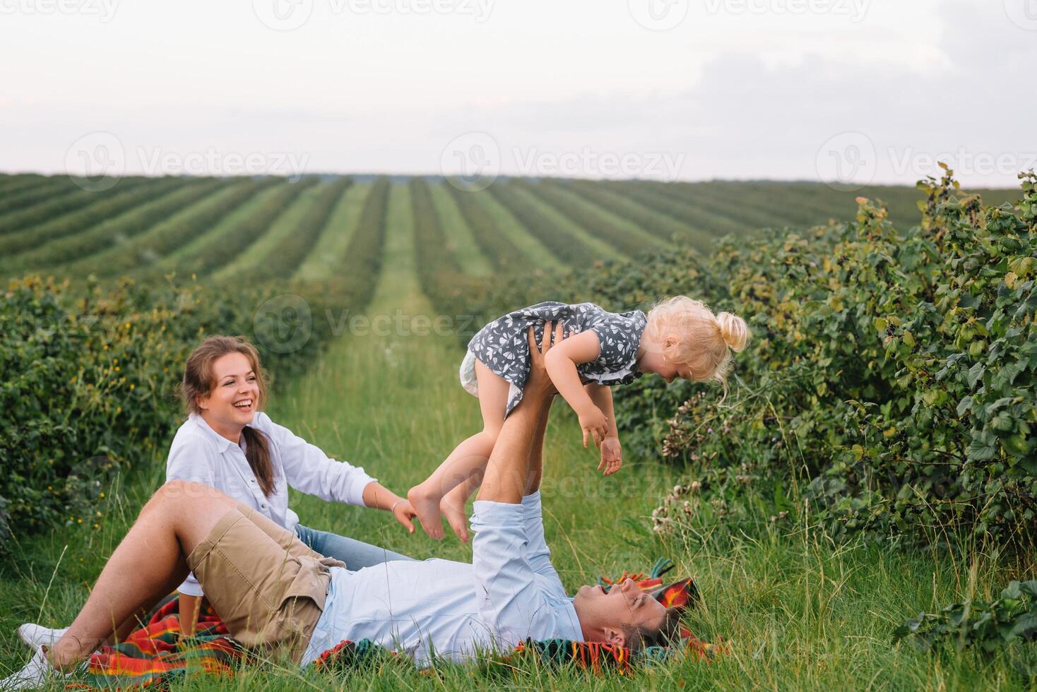 The daughter hugging parents on nature. Mom, dad and girl toddler, walk in the grass. Happy young family spending time together, outside, on vacation, outdoors. The concept of family holiday photo