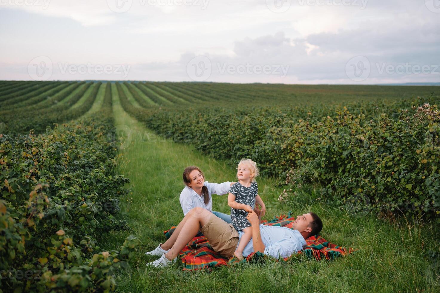 el hija abrazando padres en naturaleza. mamá, papá y niña niño pequeño, caminar en el césped. contento joven familia gasto hora juntos, afuera, en vacaciones, al aire libre. el concepto de familia fiesta foto