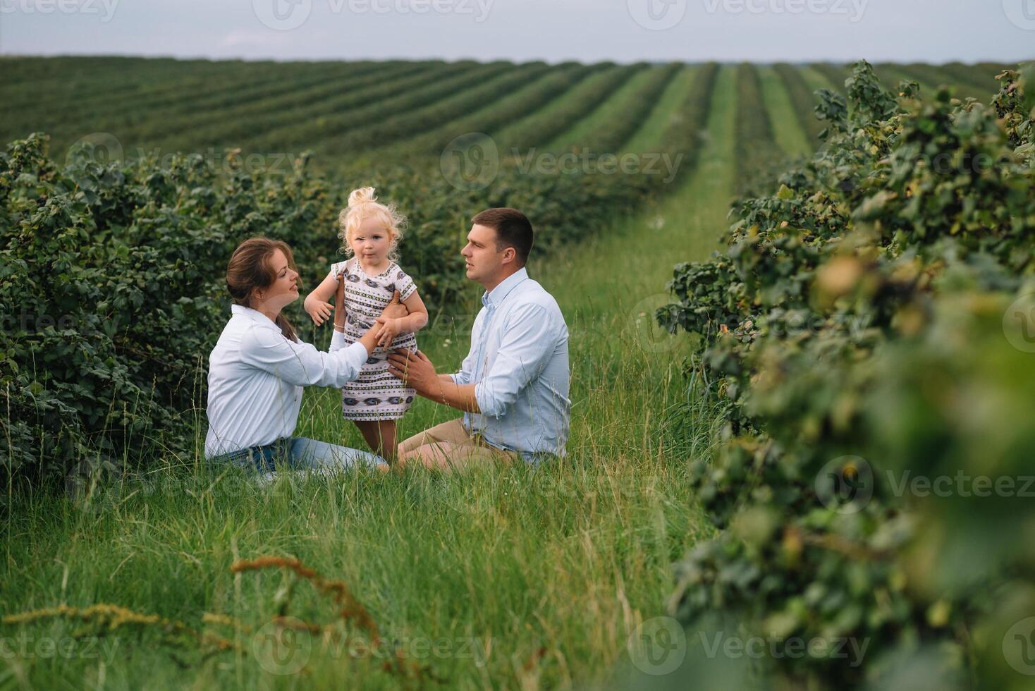 The daughter hugging parents on nature. Mom, dad and girl toddler, walk in the grass. Happy young family spending time together, outside, on vacation, outdoors. The concept of family holiday photo