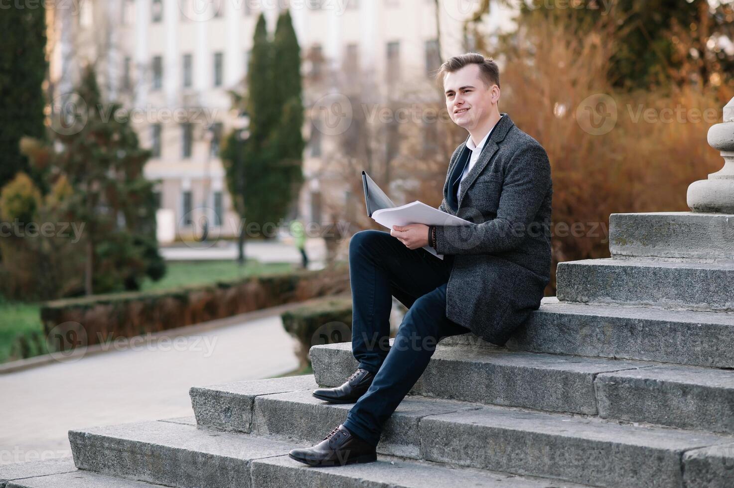 hermoso joven empresario trabajando con documentos sentado en el escalera al aire libre foto