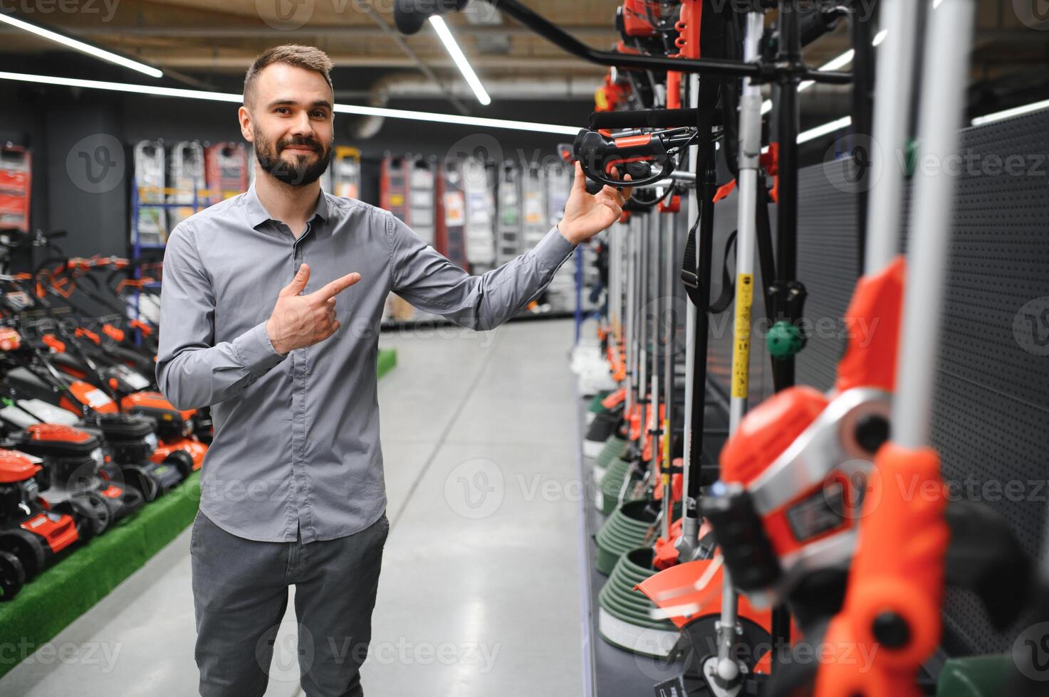a young man in a gardening equipment store chooses an electric trimmer for mowing lawn grass photo