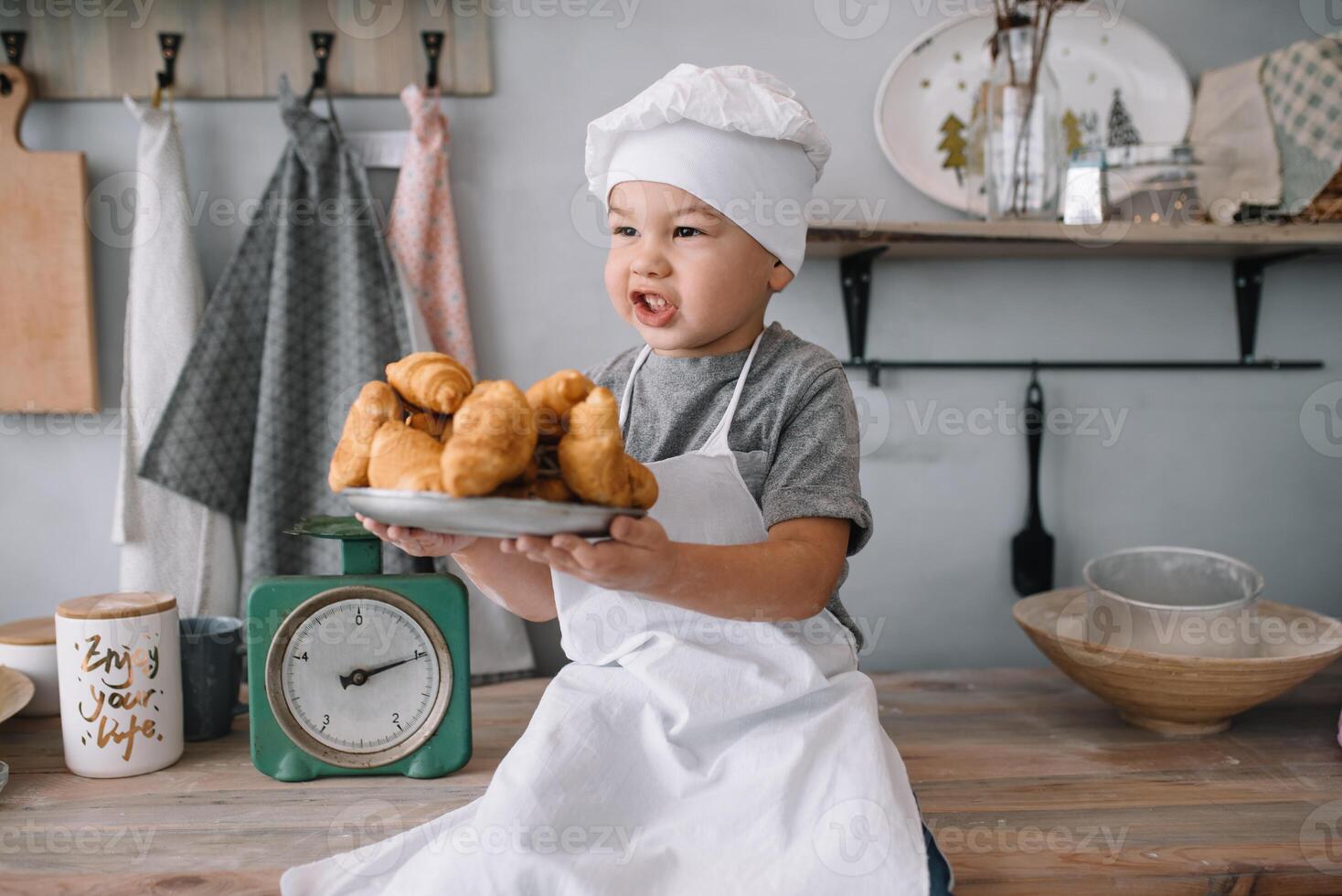 joven chico linda en el cocina cocinar cocinero en blanco uniforme y sombrero cerca mesa. hecho en casa pan de jengibre. el chico cocido el chocolate galletas. foto