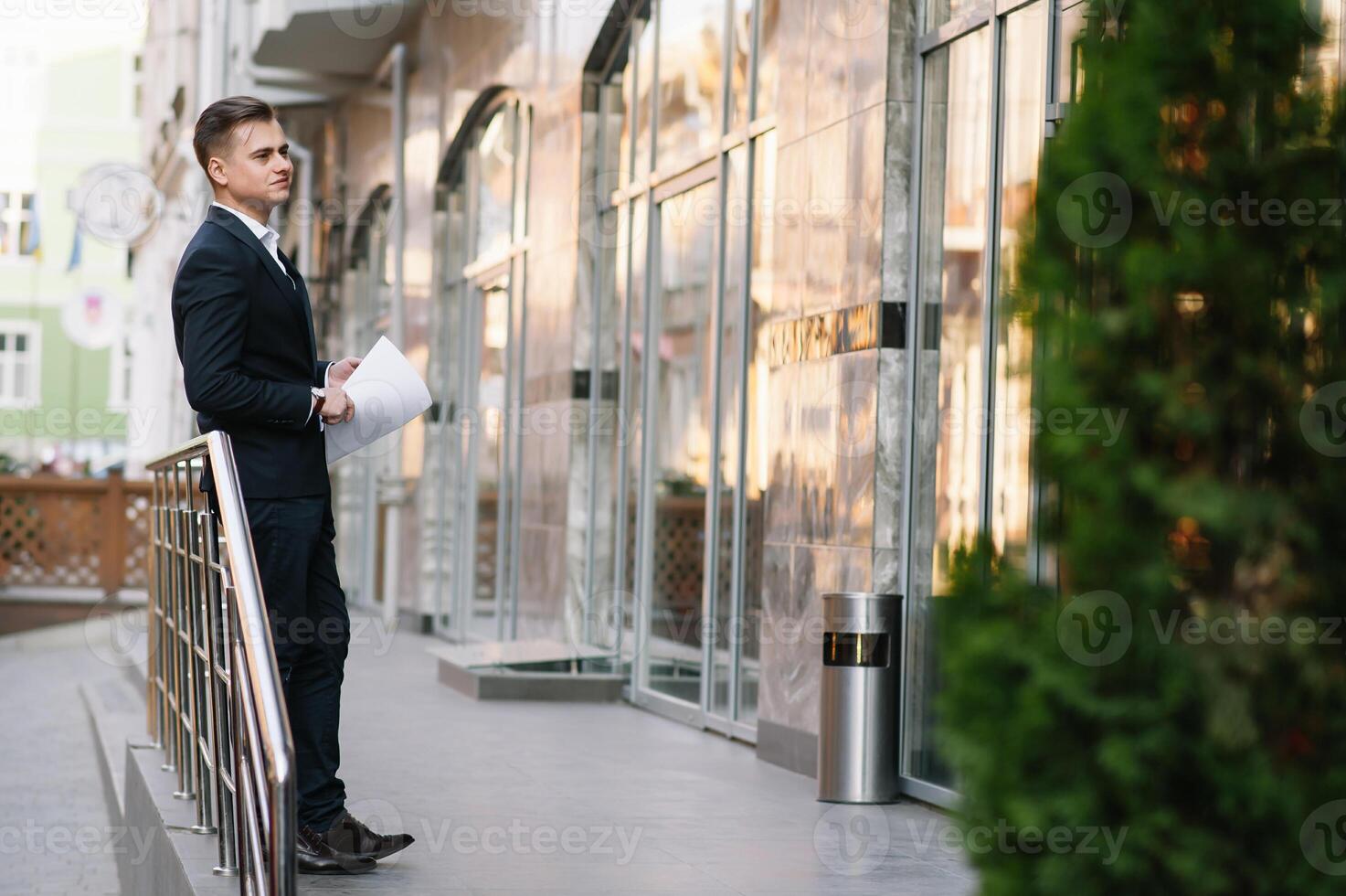 joven negocio hombre con documentos y móvil teléfono cerca de moderno edificio. foto