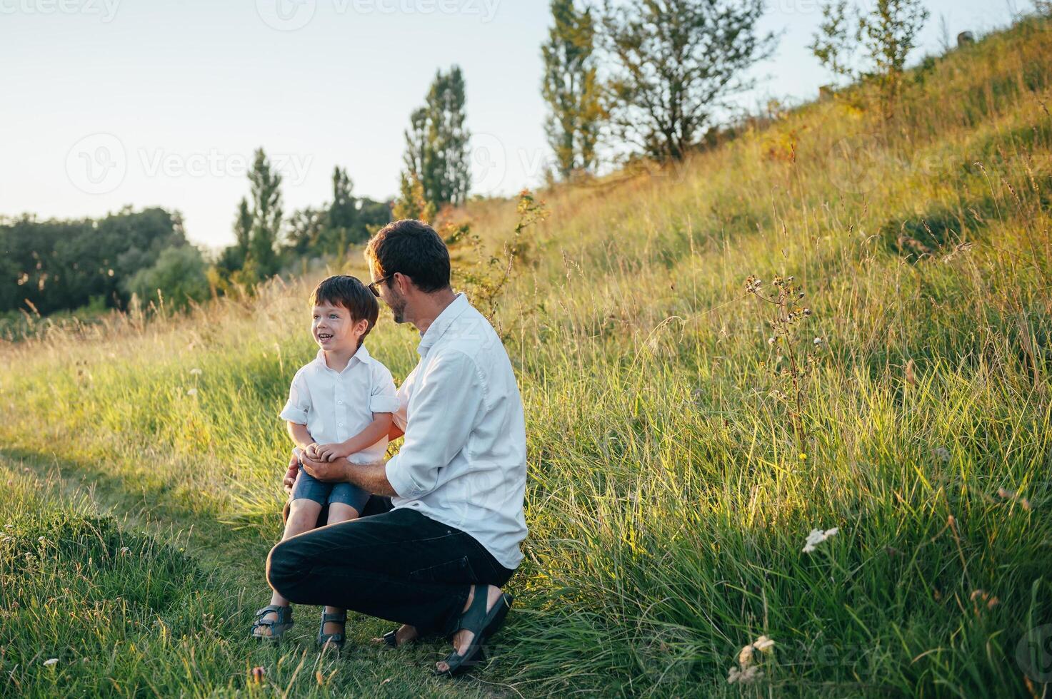 hermoso papá con su pequeño linda hijo son teniendo divertido y jugando en verde herboso césped. contento familia concepto. belleza naturaleza escena con familia al aire libre estilo de vida. familia descansando juntos. padres día. foto