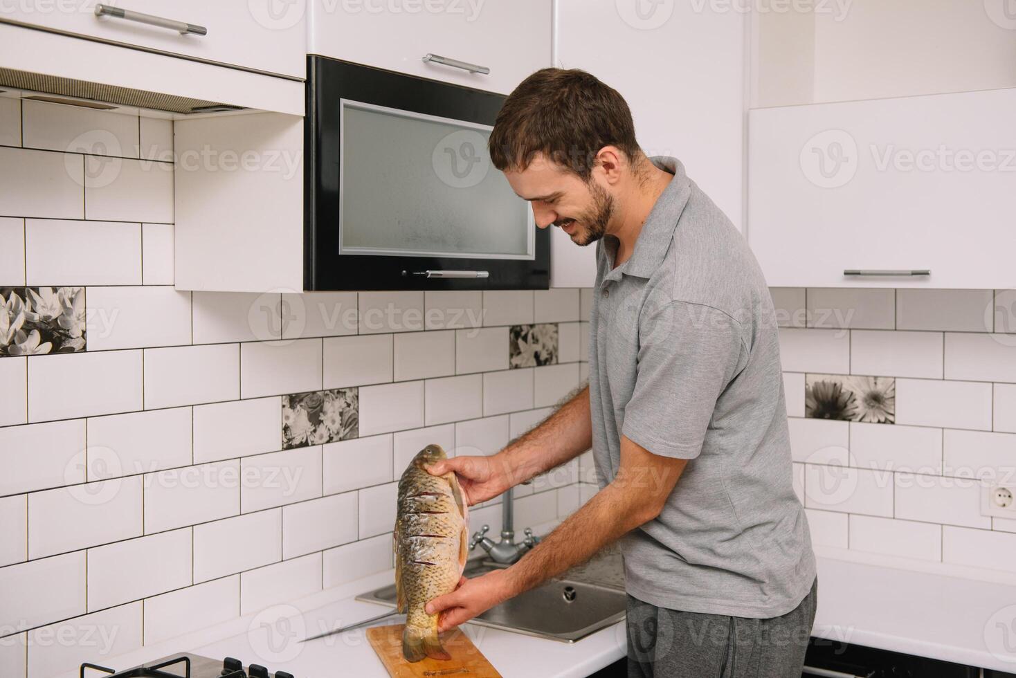 Man cutting fresh fish in kitchen in home. Man butchering fish for cook. photo