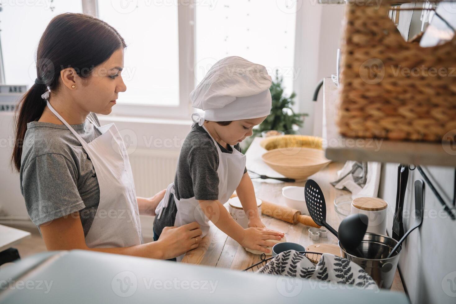 Young happy mom and her baby cook cookies at home in the kitchen. Christmas Homemade Gingerbread. cute boy with mother in white uniform and hat cooked chocolate cookies photo