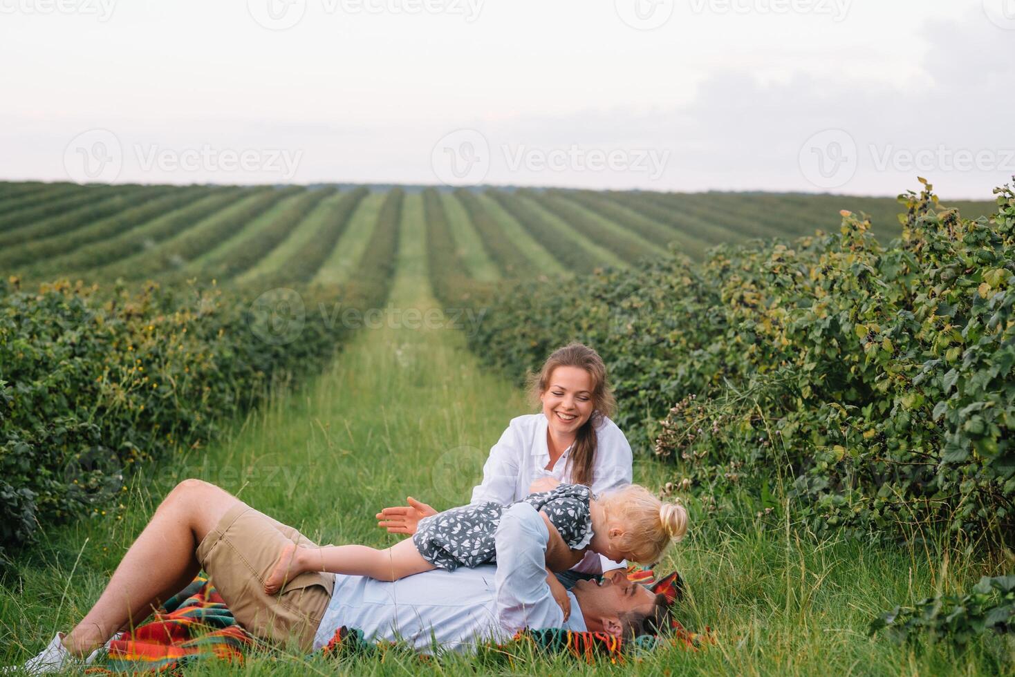 el hija abrazando padres en naturaleza. mamá, papá y niña niño pequeño, caminar en el césped. contento joven familia gasto hora juntos, afuera, en vacaciones, al aire libre. el concepto de familia fiesta foto