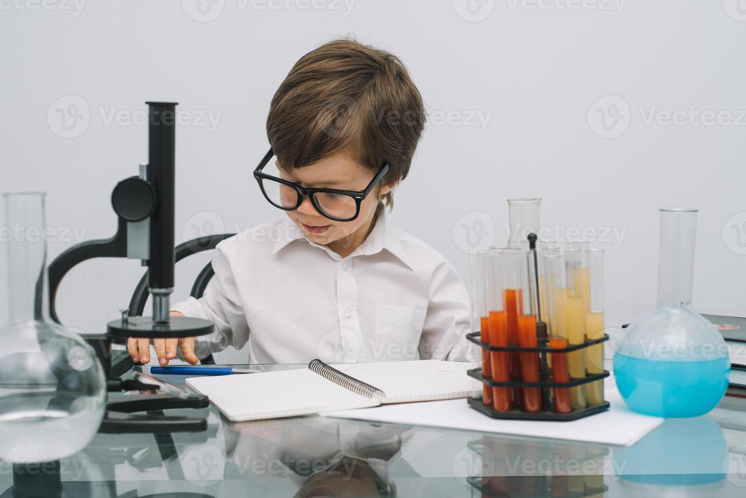 el chico con un microscopio y varios vistoso matraces en un blanco antecedentes. un chico haciendo experimentos en el laboratorio. explosión en el laboratorio. Ciencias y educación foto