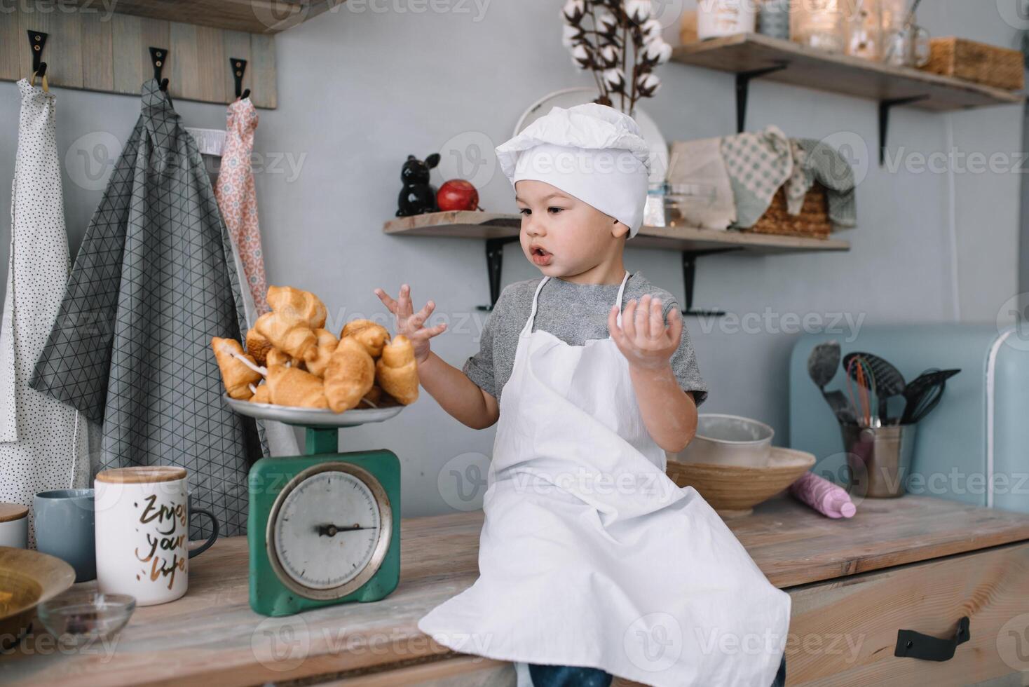 joven chico linda en el cocina cocinar cocinero en blanco uniforme y sombrero cerca mesa. hecho en casa pan de jengibre. el chico cocido el chocolate galletas. foto