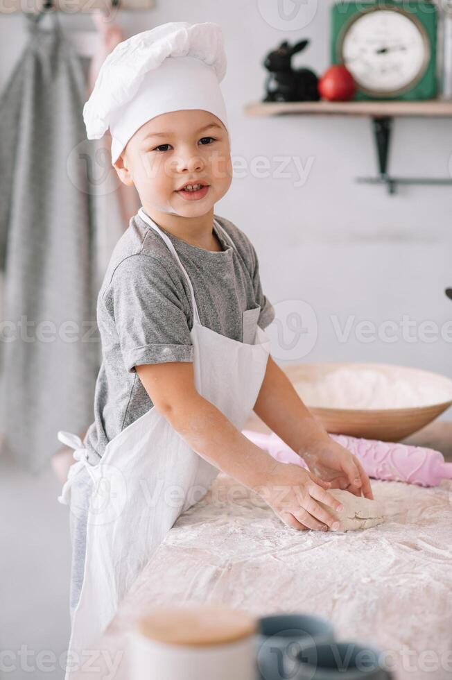 joven chico linda en el cocina cocinar cocinero en blanco uniforme y sombrero cerca mesa. hecho en casa pan de jengibre. el chico cocido el chocolate galletas foto