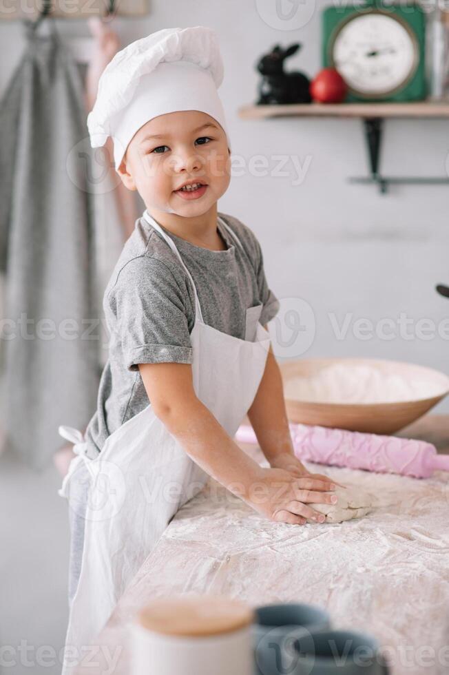 joven chico linda en el cocina cocinar cocinero en blanco uniforme y sombrero cerca mesa. hecho en casa pan de jengibre. el chico cocido el chocolate galletas foto